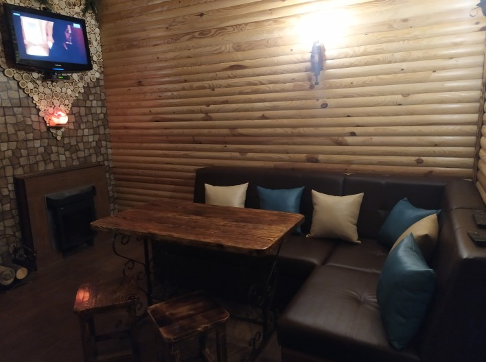 Комната отдыха с камином на дровах,плазменным телевизором,мягкой мебелью и столом для трапезы.